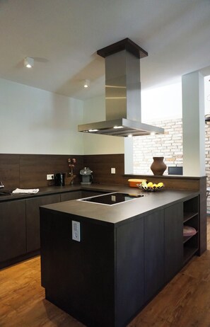 A modern kitchen with a central island, dark cabinetry, and a brick wall. - New large premium vacation apartment in the Hinterstoder ski/hiking area with terrace (Hinterstoder)