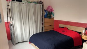 A bedroom with a bed, a wooden dresser, a wardrobe, and a curtain.