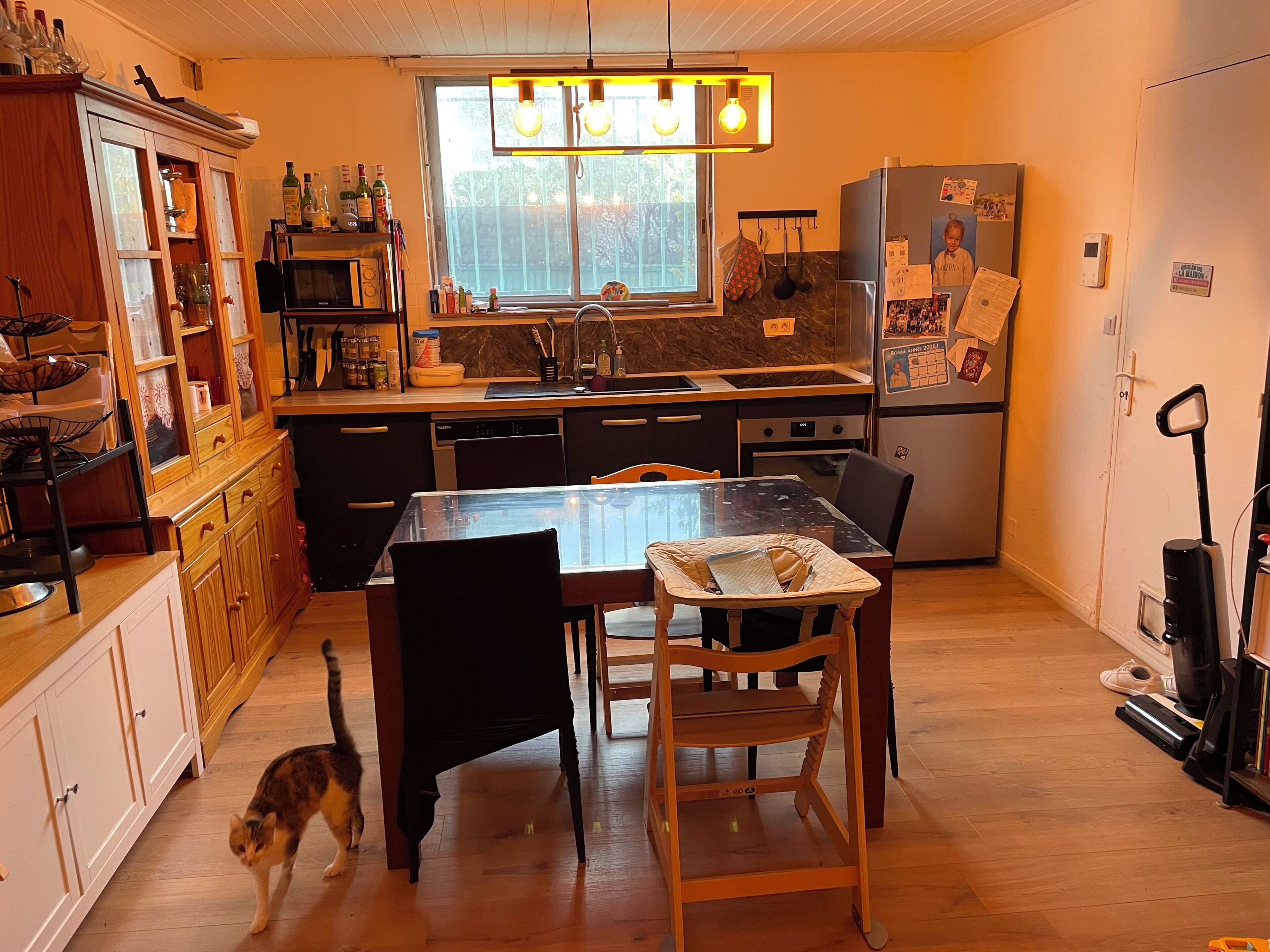 Ett modernt kök med träskåp, ett matbord i glas och en inbyggd ugn.