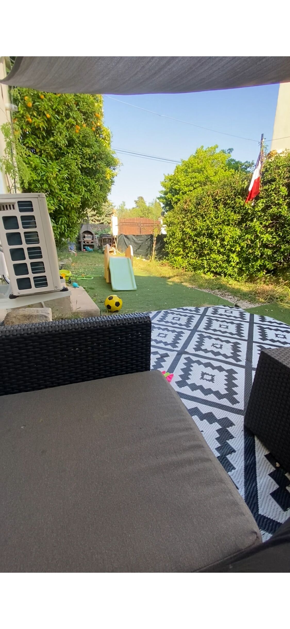 Eine Terrasse mit einer Sitzecke, einem gemusterten Teppich und einer Spielanlage im Hintergrund.