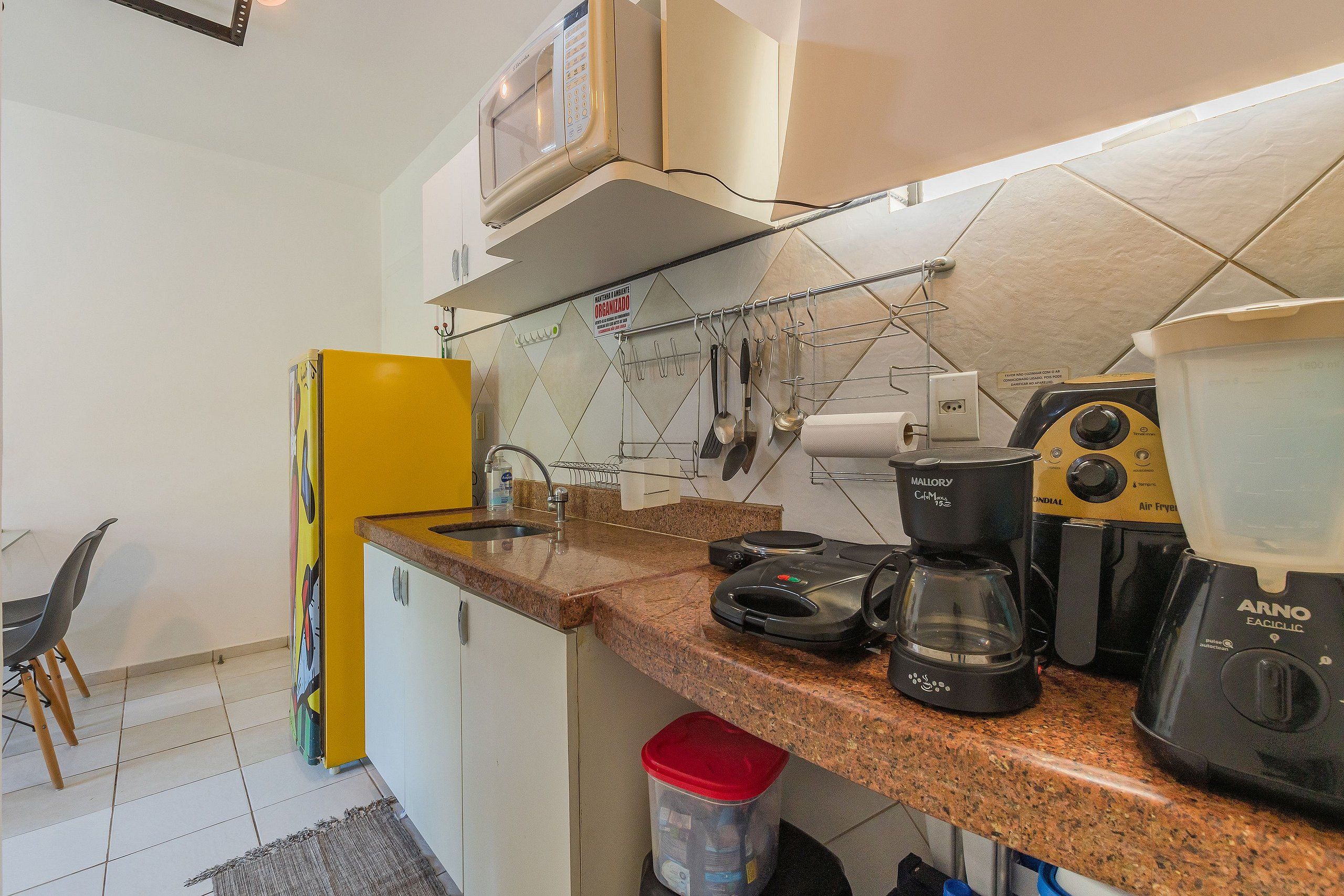 Cocina compacta con microondas, cafetera y licuadora en la encimera.