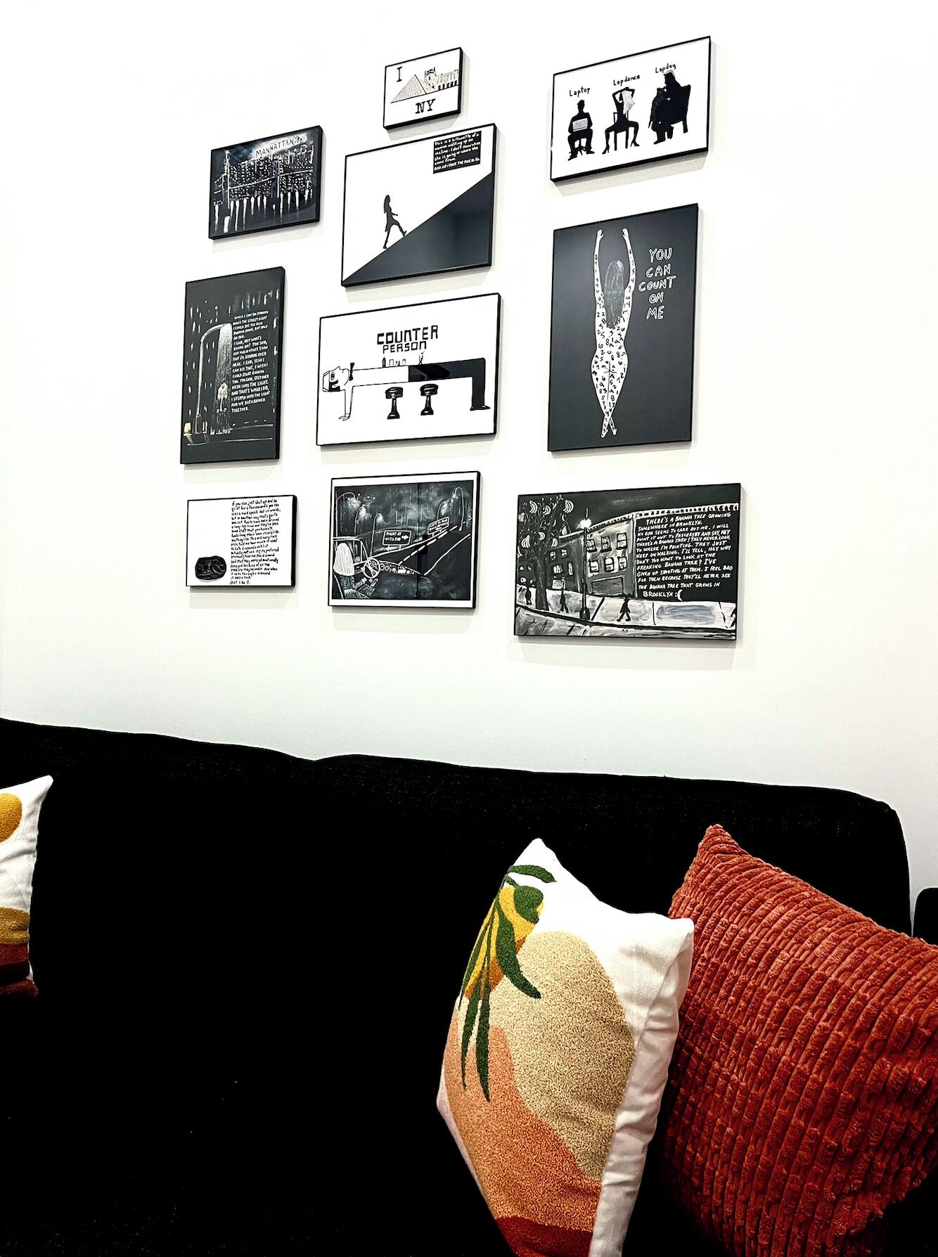 Una pared decorada con varias obras de arte enmarcadas y un sofá negro con cojines rojos y blancos.