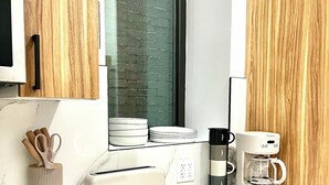 A modern kitchen with wooden cabinets, a white countertop, a toaster, a coffee maker, and a window with a brick wall view. - Hudson Yards Modern 1 bedroom (New York)