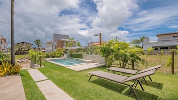 Un patio trasero con piscina, sillas de descanso y un césped bien cuidado.
