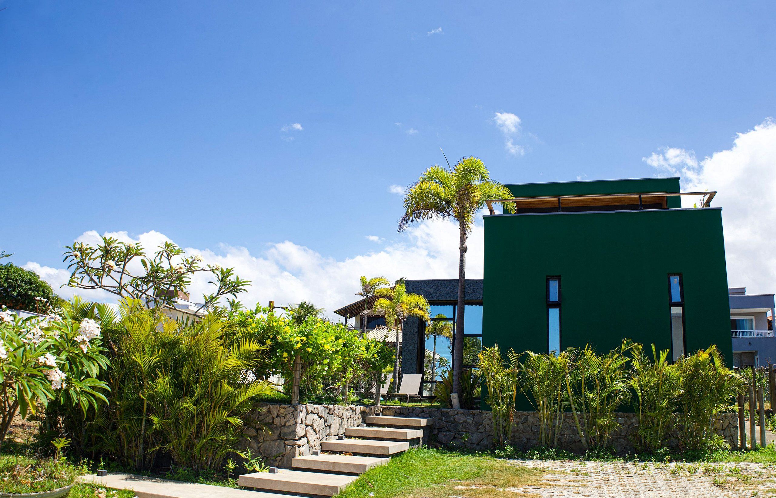A modern building with a green facade, a stone staircase leading to the entrance, and tropical vegetation around.
