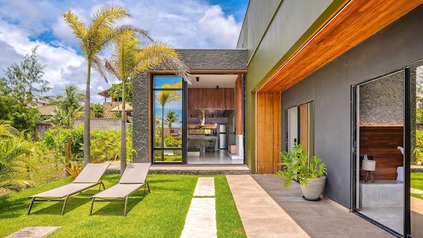 Ein modernes Haus mit Terrasse, zwei Liegestühlen, einem Blumentopf und Blick ins Innere.
