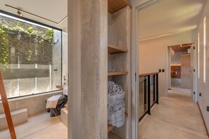 A modern bathroom with a large window, a concrete column, and a wooden bench.