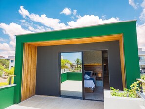 Een modern gebouw met een groene buitenkant, een schuifdeur die leidt naar een kamer met een bed en een klein zithoekje.