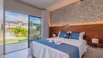 A bedroom with a large bed, a wooden headboard, a view of the outdoors, and a small table with a lamp.