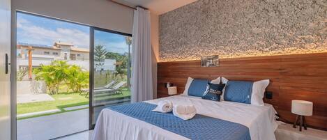 A bedroom with a large bed, a wooden headboard, a view of the outdoors, and a small table with a lamp.