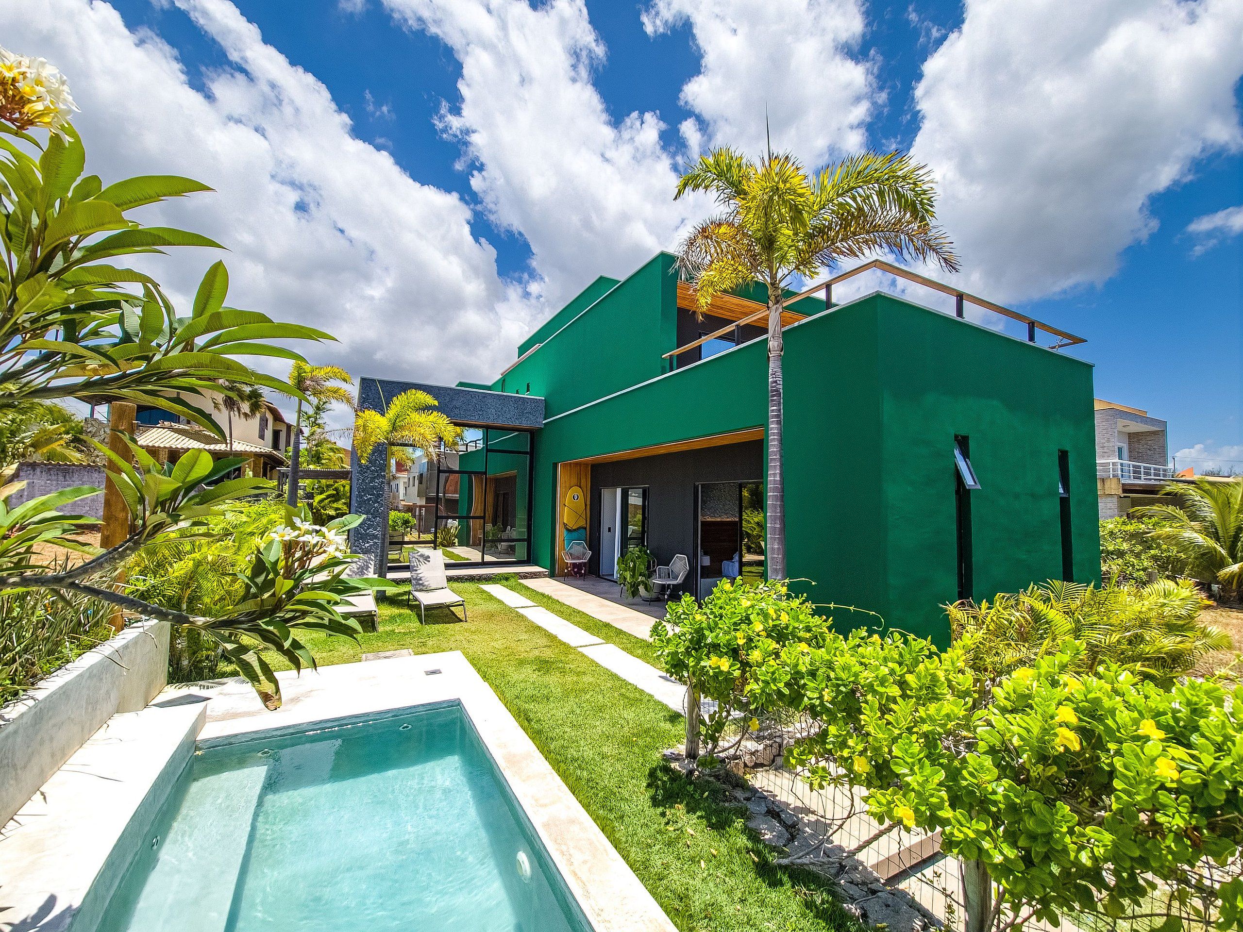 Uma casa moderna com piscina, fachada verde e plantas tropicais.