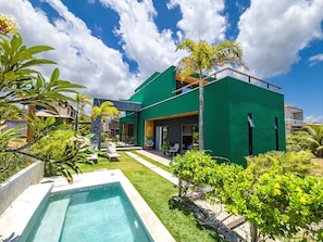 A modern house with a swimming pool, green exterior, and tropical plants.