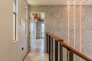 Un pasillo con barandilla de madera, pared con textura y una silla al fondo.