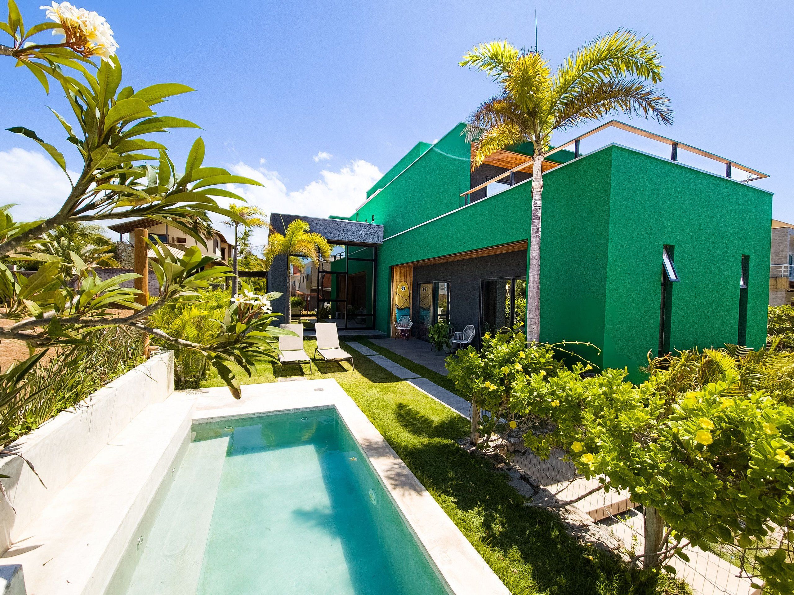 A modern house with a swimming pool, green exterior, and a patio area.