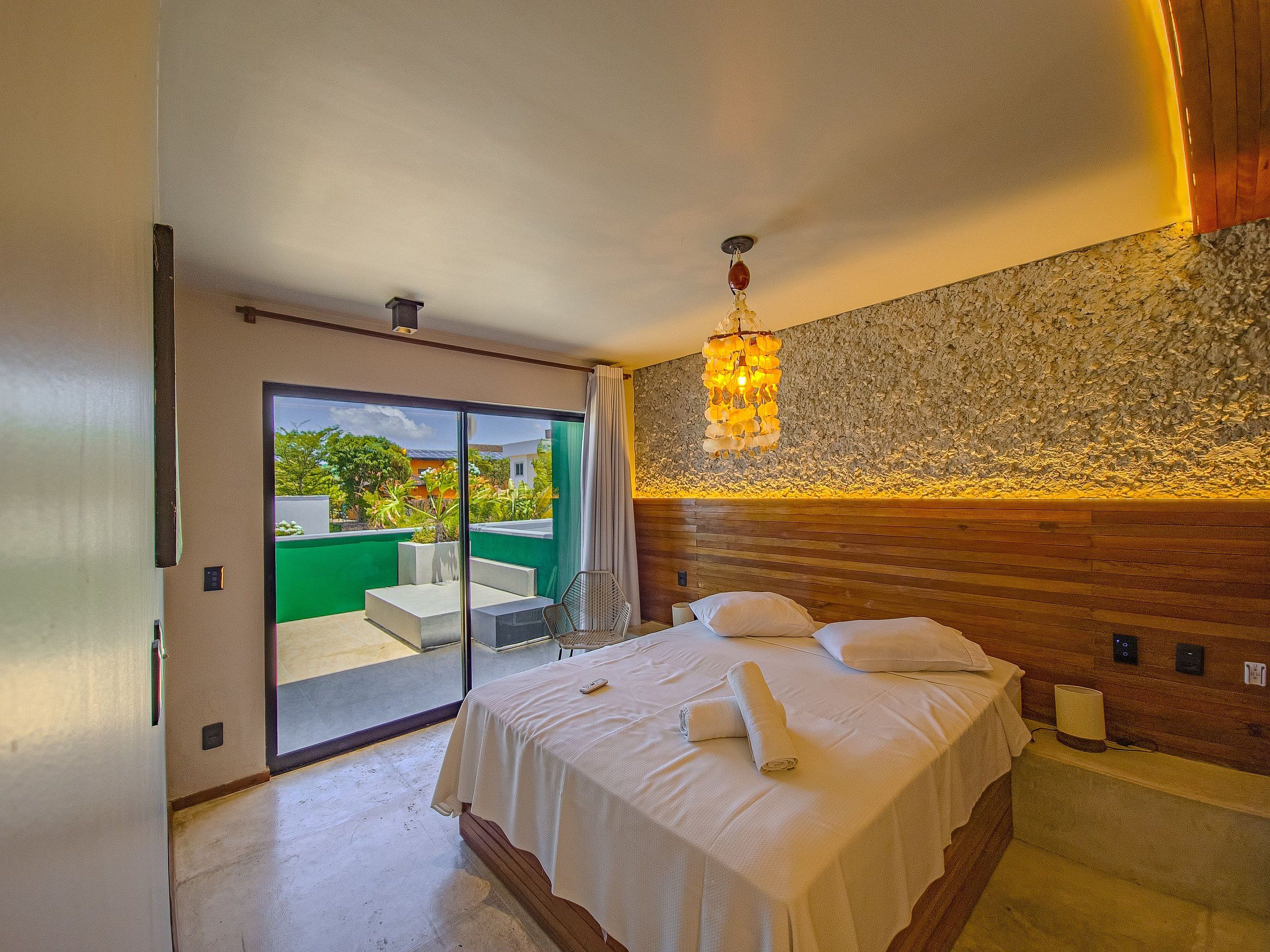 Un dormitorio con cama, mesita de noche, lámpara y vistas al exterior.
