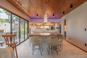A modern kitchen with a large island, wooden ceiling, and large windows.