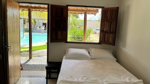 Ein Schlafzimmer mit Bett, einem Fenster mit Holzklappläden und Blick auf einen Swimmingpool.