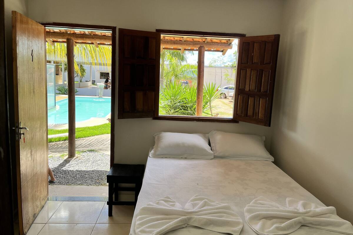 Une chambre avec un lit, une fenêtre avec des volets en bois et une vue sur une piscine.