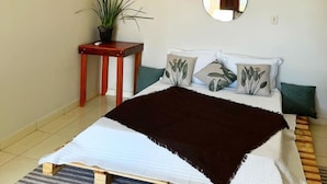 Ein Schlafzimmer mit Bett, Nachttisch, Topfpflanze, Spiegel und Klimaanlage.