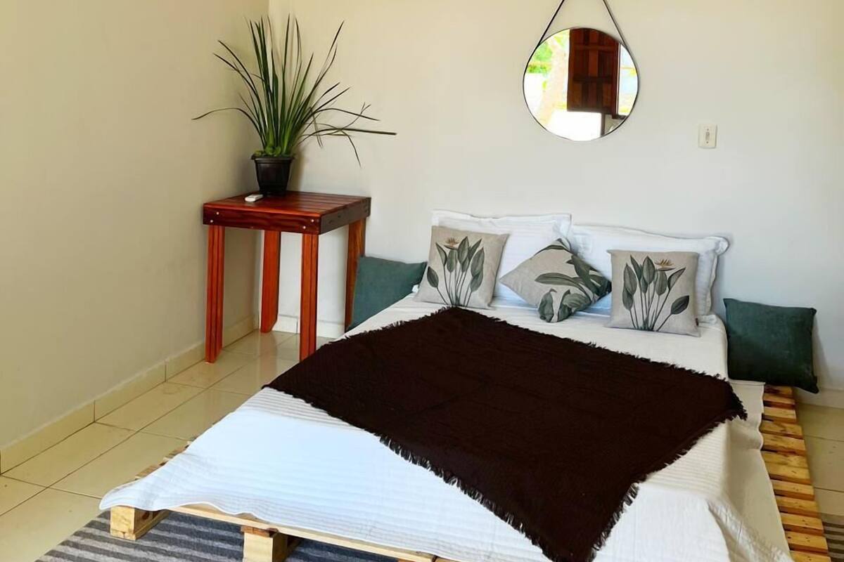 Une chambre à coucher comprenant un lit, une table de chevet, une plante en pot, un miroir et un appareil de climatisation.