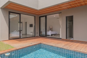 Une chambre d’hôtel moderne dotée d’une grande porte-fenêtre coulissante, d’une terrasse en bois et d’un petit espace piscine.