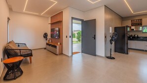 Een moderne woonkamer met een bank, een tafel, een televisie en een keukenhoek met een koelkast en kastjes.