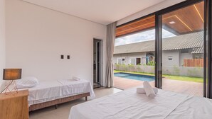Een moderne hotelkamer met twee bedden, een houten nachtkastje, een lamp en uitzicht op een zwembad.