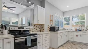 A modern kitchen with white cabinets, a black stove, a microwave, and a tiled backsplash. - Beach Bungalow w/ Pool & Hot Tub. Casinos nearby! (Biloxi)