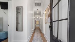 Un corridoio con pareti bianche, pavimento in legno e tappeto grigio. Da entrambe le parti si aprono porte, una con cornice nera e l'altra con cornice argentata.