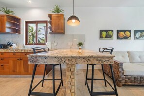 A kitchen with a marble countertop, wooden cabinets, a stone pillar, and a hanging pendant light. - New Luxury Apt  | Quiet Sac Bajo | Private Dock (Isla Mujeres)