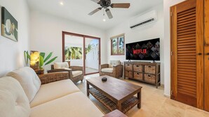 Ein Wohnzimmer mit einer Couch, einem Couchtisch, Korbstühlen, einem Fernseher und einem Deckenventilator.