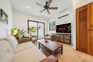 A living room with a sofa, coffee table, wicker chairs, a TV, and a ceiling fan. - New Luxury Apt  | Quiet Sac Bajo | Private Dock (Isla Mujeres)