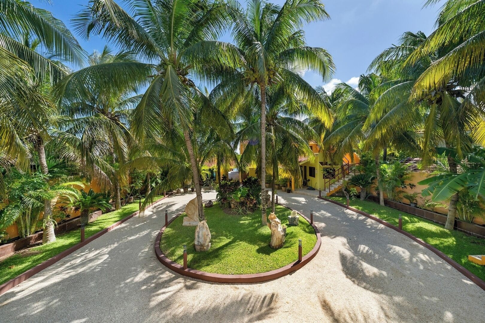 A tropical resort with palm trees, a central circular garden, and a yellow building.