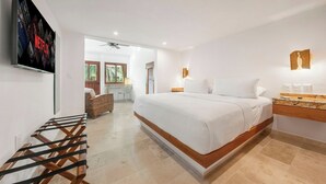 Ein modernes Hotelzimmer mit einem großen Bett, einem an der Wand montierten Fernseher, einem Schreibtisch mit Computer und einem Fenster mit Blick auf Palmen.