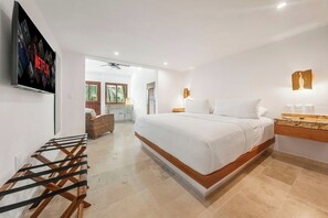 A modern hotel room with a large bed, a TV mounted on the wall, a desk with a computer, and a window with a view of palm trees. - New Luxury Apt  | Quiet Sac Bajo | Private Dock (Isla Mujeres)