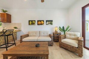 A living room with a sofa, two side tables, a coffee table, and a dining area with a bar stool. - New Luxury Apt  | Quiet Sac Bajo | Private Dock (Isla Mujeres)