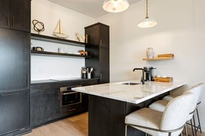 Moderni keittiö, jossa on tummat kaapit, marmorinen keittiösaareke ja baarituolit.