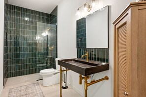 Ein Badezimmer mit einem dunklen Waschbecken, einer weißen Toilette und grünen Fliesenwänden.