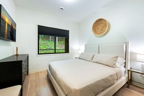 Quarto com cama, janela com vista para vegetação, obra de arte na parede e mesa de cabeceira.