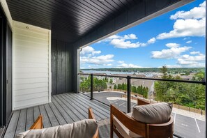 A balcony with a view of a lake and buildings, wooden furniture, and a railing. - Luna View | Top-Floor Water Views & Covered Patio in Sister Bay (Sister Bay)