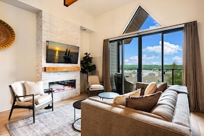 A living room with a fireplace, a sofa, a chair, a table, and a large window with a view. - Luna View | Top-Floor Water Views & Covered Patio in Sister Bay (Sister Bay)