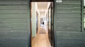 Un pasillo con piso de madera, un tapete y una puerta con el número 303.