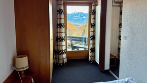 Ett hotellrum med ett träpanelat tak, en säng, en lampa och utsikt över bergen genom ett fönster med mönstrade gardiner.