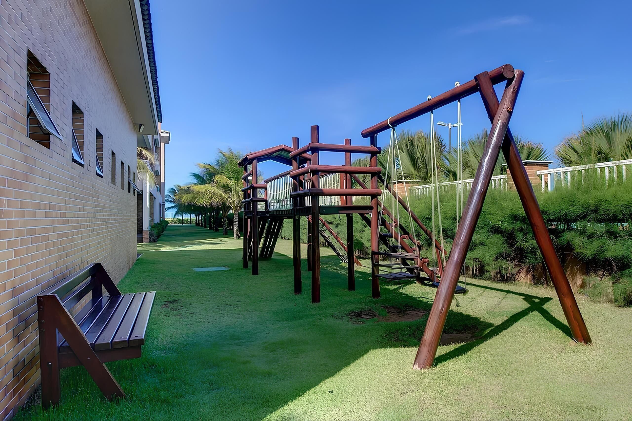 Ein Spielplatz mit Holzkonstruktionen und einer Bank vor einem Backsteinhaus.