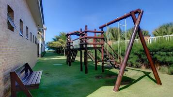 Ein Spielplatz mit Holzkonstruktionen und einer Bank vor einem Backsteinhaus.