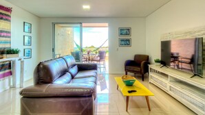 A living room with a brown leather sofa, a yellow coffee table, and a flat-screen TV on a white stand.