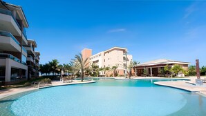 A large swimming pool with a clear blue water, surrounded by palm trees and modern buildings.