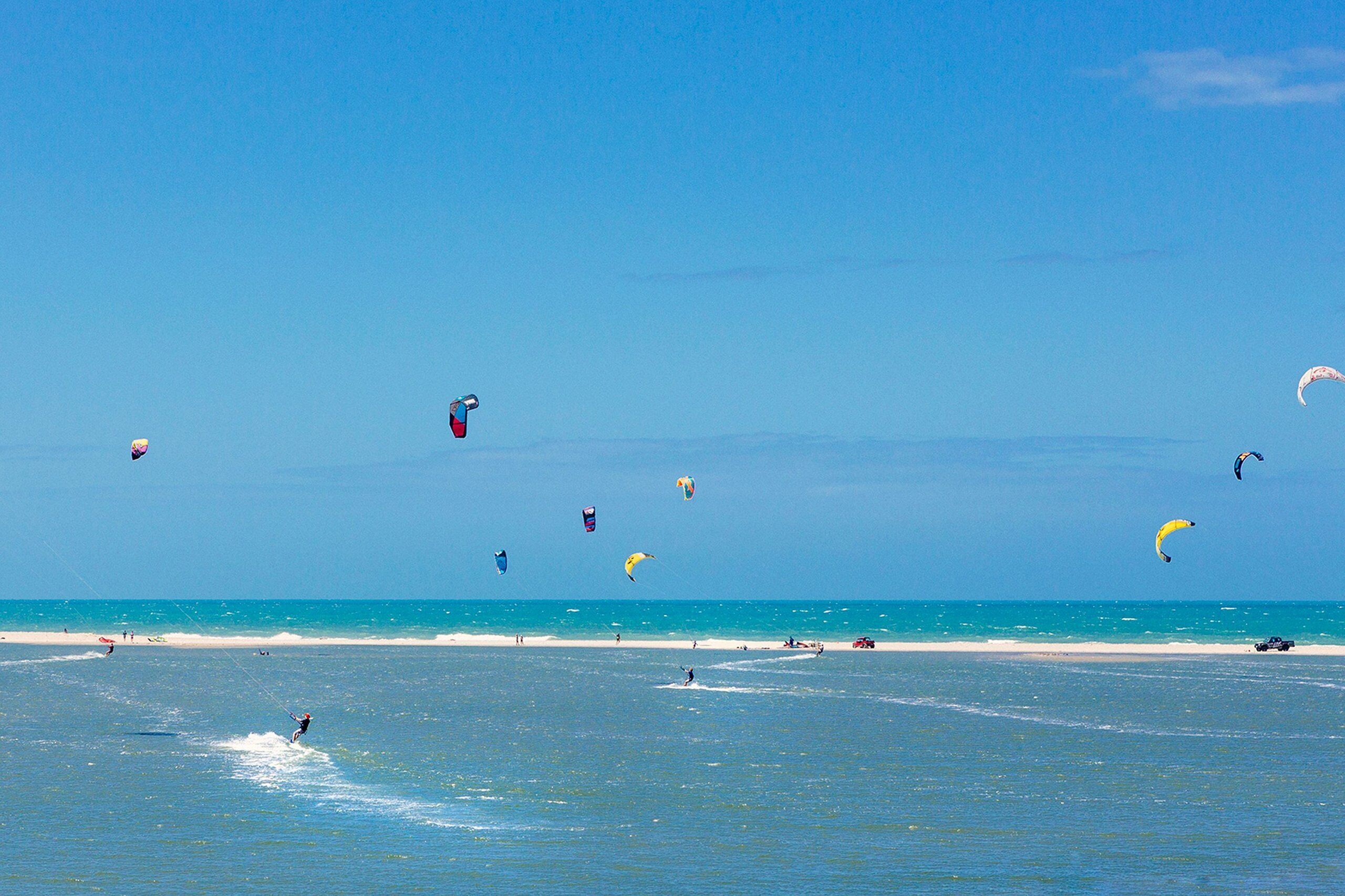 Ein Strand mit blauem Himmel und mehreren Drachen in der Luft.