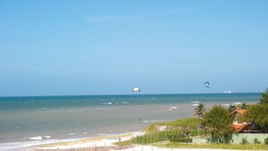A beach with a view of the ocean, a kite surfer, and a distant city skyline.