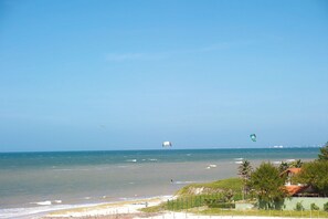 Une plage avec vue sur l’océan, un pratiquant de kitesurf et, au loin, le profil d’une ville.